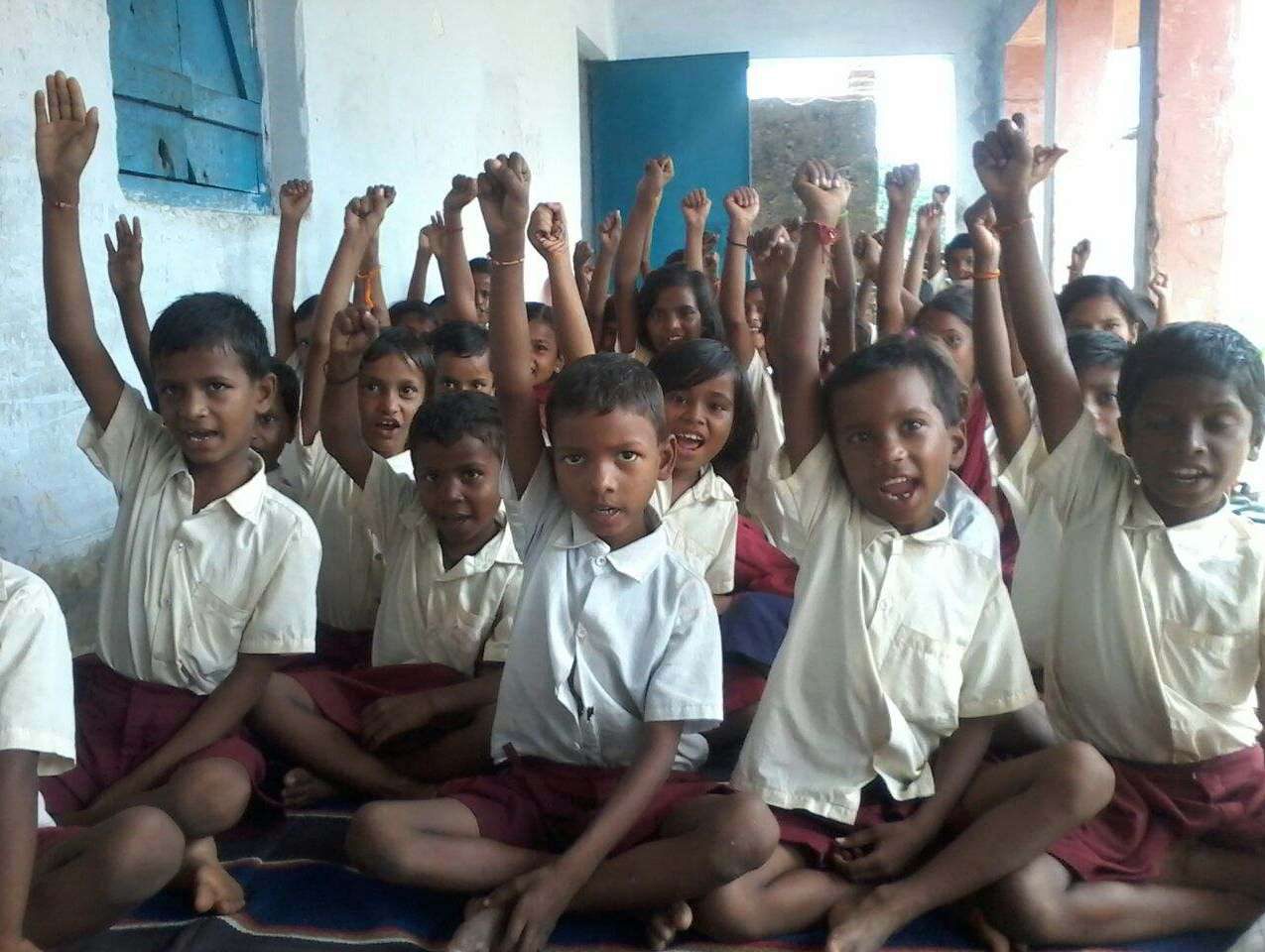 Schoolchildren in uniform raise their hands in a village classroom in Koderma